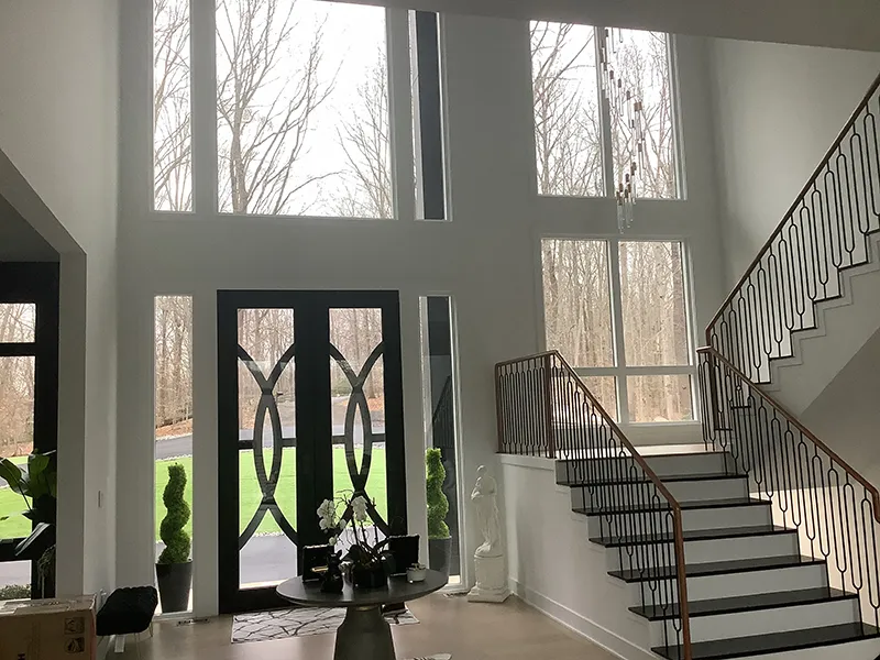 Modern foyer with tall windows, decorative door, and elegant staircase.