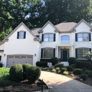 Two-story white house with a light gray roof, seen from the rear. Green trees surround it under an overcast sky