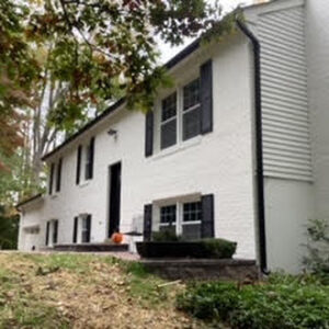 image shows a white, two-story house with black shutters and a black roof