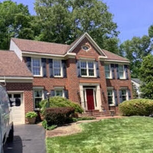image shows a two-story brick house with a brown shingled roof