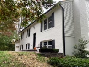 image shows a two-story house has a white brick facade, black shutters, and a newer roof