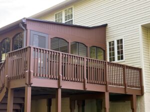 image shows the exterior of a house featuring a brown wooden deck and a sunroom