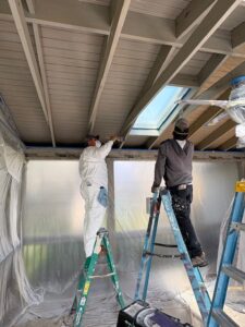 image shows two painters on ladders painting the ceiling of a screened-in porch